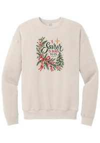 A Savior Is Born To Us crewneck sweatshirt in Heather Dust, featuring watercolor evergreen and holly with a red ribbon bow, the words A Savior is born to us, and Isaiah 9:6