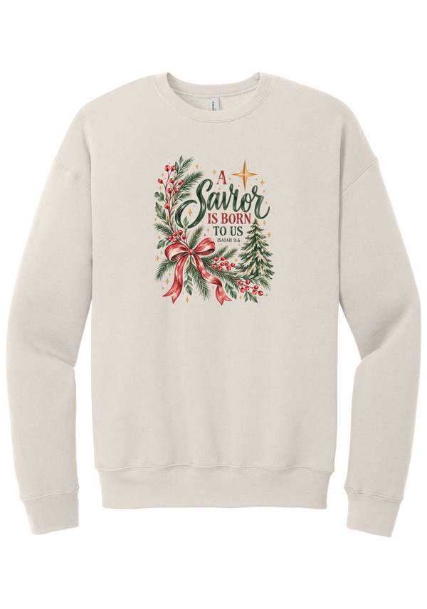 A Savior Is Born To Us crewneck sweatshirt in Heather Dust, featuring watercolor evergreen and holly with a red ribbon bow, the words A Savior is born to us, and Isaiah 9:6