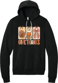 Give Thanks Coquette hoodie in Black, featuring three bow-topped stamp panels with a turkey, stacked pumpkins, and a pink bow above Give Thanks in patchwork letters