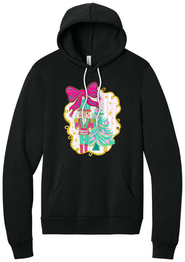 Nutcracker Bow hoodie in Black, featuring a teal and pink nutcracker beside a tinsel tree under a big hot pink bow