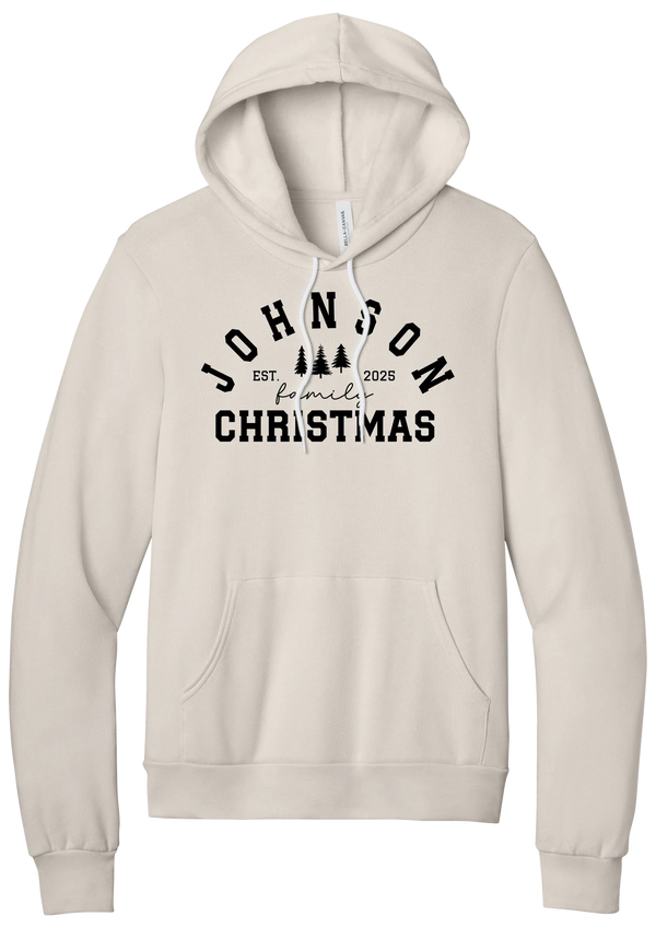 Personalized Family Christmas hoodie in Heather Dust, featuring an arched family name over pine trees with EST. year and family Christmas lettering