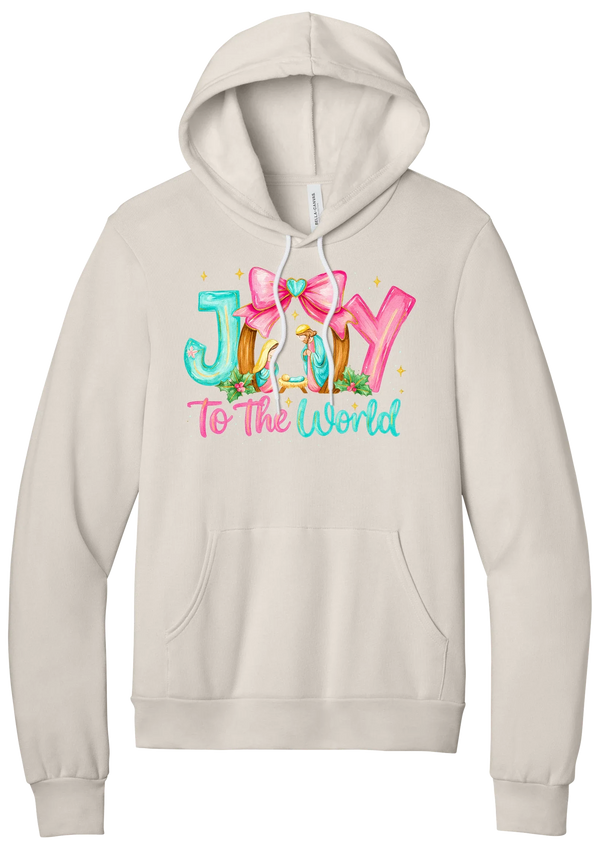 Joy to the World Nativity hoodie in Heather Dust, featuring painted JOY letters framing a nativity scene with a pink bow and To The World script