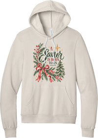 A Savior Is Born To Us hoodie in Heather Dust, featuring watercolor evergreen and holly with a red ribbon bow, the words A Savior is born to us, and Isaiah 9:6