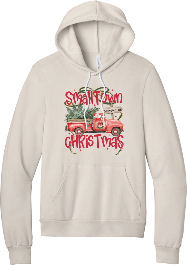 Personalized Small Town Christmas hoodie in Heather Dust, featuring Santa in a vintage red pickup truck hauling a Christmas tree past a personalized town road sign, with red Small Town Christmas lettering