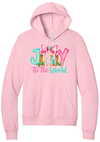 Joy to the World Nativity hoodie in Pink, featuring painted JOY letters framing a nativity scene with a pink bow and To The World script