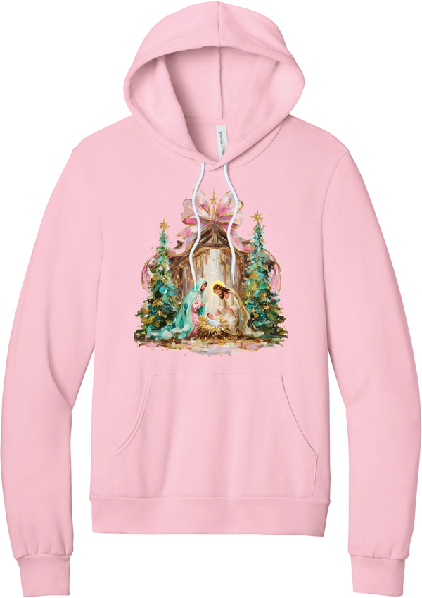 Painterly Nativity hoodie in Pink, featuring a painterly nativity scene with Mary, Joseph, and baby Jesus in a wooden stable between teal Christmas trees and a pink bow
