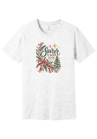 A Savior Is Born To Us tee in Ash, featuring watercolor evergreen, holly, and a red ribbon bow with hand-lettered A Savior is born to us and Isaiah 9:6