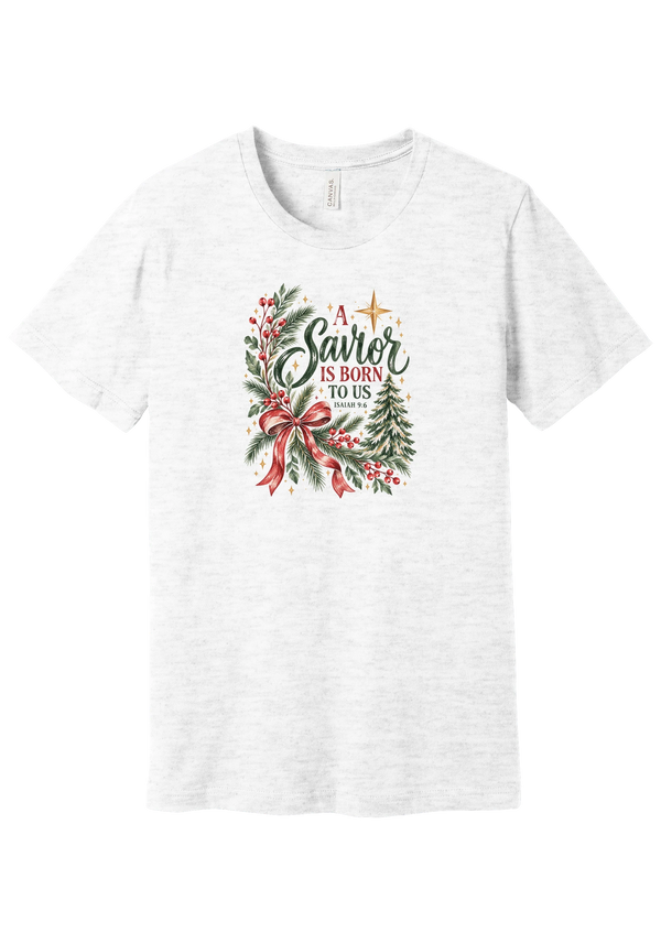 A Savior Is Born To Us tee in Ash, featuring watercolor evergreen, holly, and a red ribbon bow with hand-lettered A Savior is born to us and Isaiah 9:6