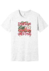 Personalized Small Town Christmas tee in Ash, featuring Santa in a vintage red pickup hauling a Christmas tree past a road sign personalized with your town