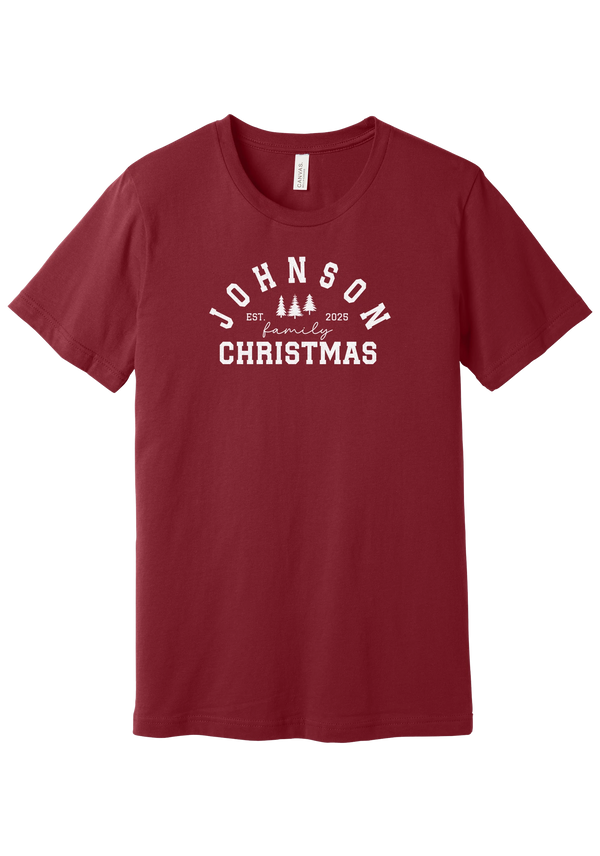 Personalized Family Christmas tee in Cardinal, featuring a personalized family last name arched over three pine trees with EST. and the year