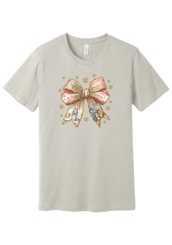 Nativity Bow tee in Dust, featuring a blush satin bow with painted nativity scenes in its ribbons and gold snowflakes