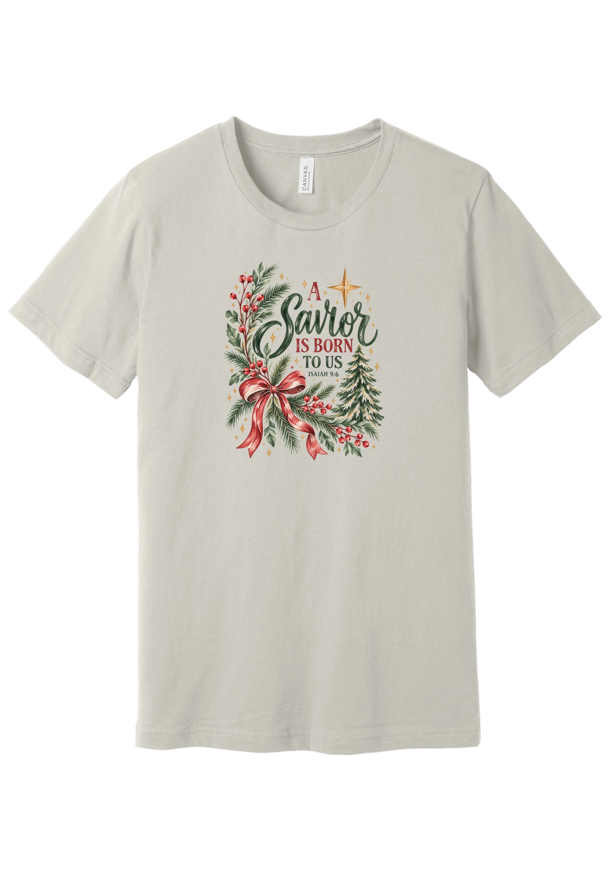 A Savior Is Born To Us tee in Dust, featuring watercolor evergreen, holly, and a red ribbon bow with hand-lettered A Savior is born to us and Isaiah 9:6