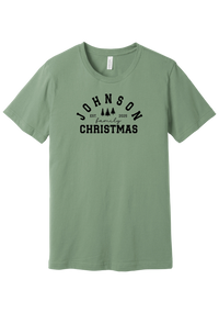 Personalized Family Christmas tee in Sage, featuring a personalized family last name arched over three pine trees with EST. and the year