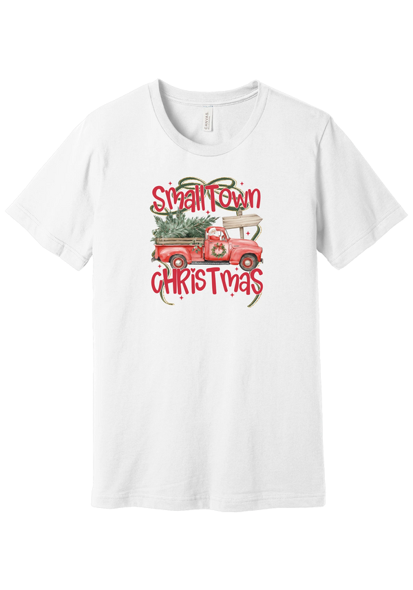 Personalized Small Town Christmas tee in White, featuring Santa in a vintage red pickup hauling a Christmas tree past a road sign personalized with your town